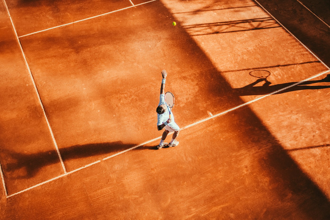 A tennis court seen from above, with one player serving